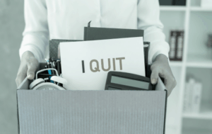 A person quitting their job, carrying a box of belongings and a sign that says, "I quit"