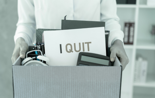 A person quitting their job, carrying a box of belongings and a sign that says, "I quit"